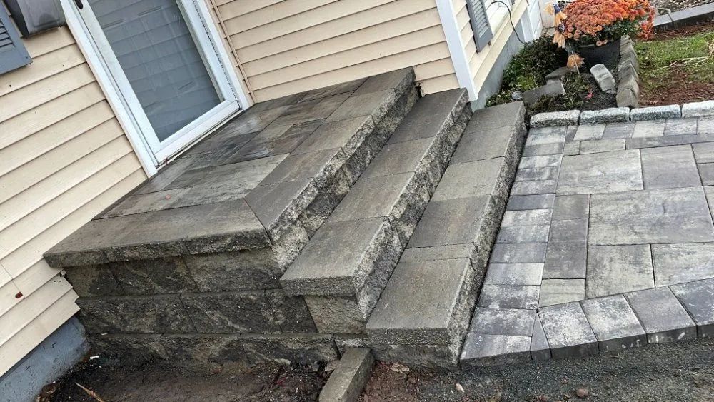 Stone steps leading up to a house entrance with a brick patio on the side.