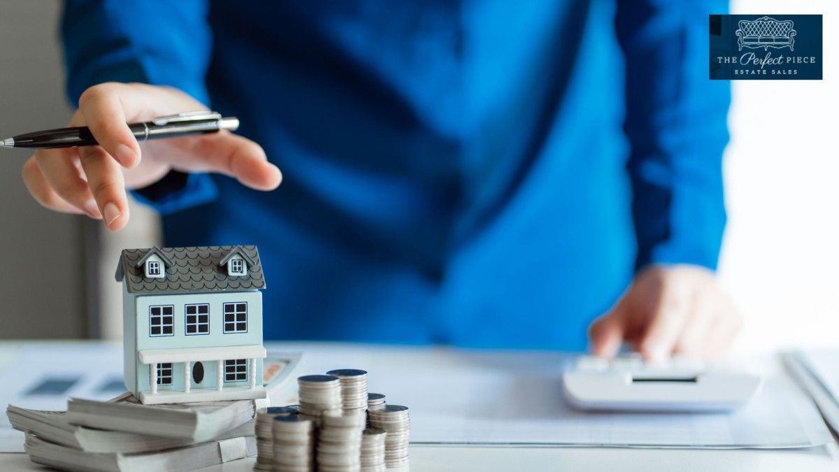 A person is sitting at a table with a model house and stacks of coins.