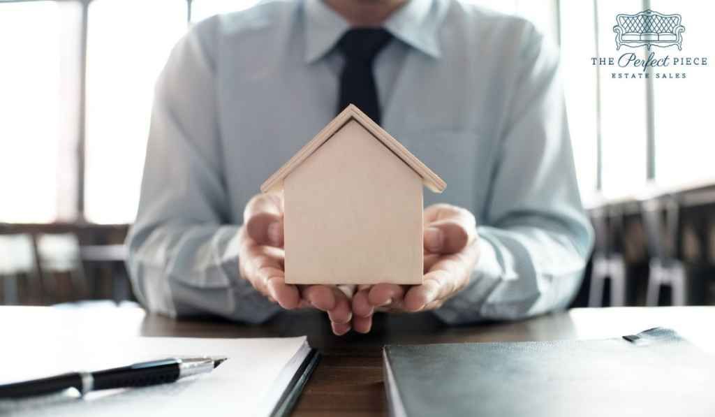 A man in a suit and tie is holding a small wooden house in his hands.