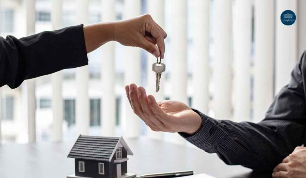 A woman is handing a key to a man in front of a model house.