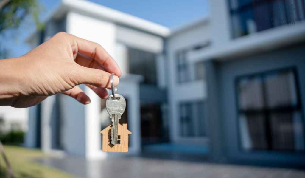 A person is holding a key in front of a house.