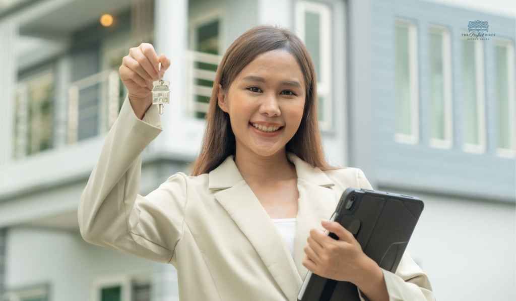 A woman is holding a tablet and a key in front of a house.