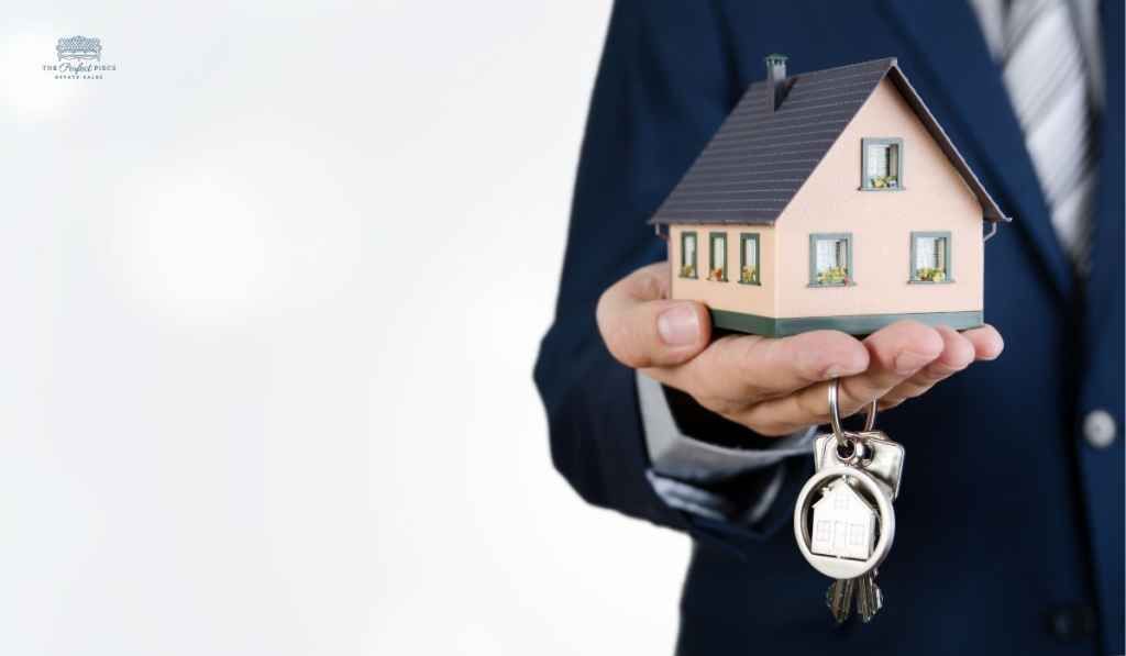 A man in a suit is holding a model house and keys.