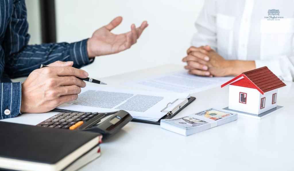 A man and a woman are sitting at a table with a model house and a calculator.