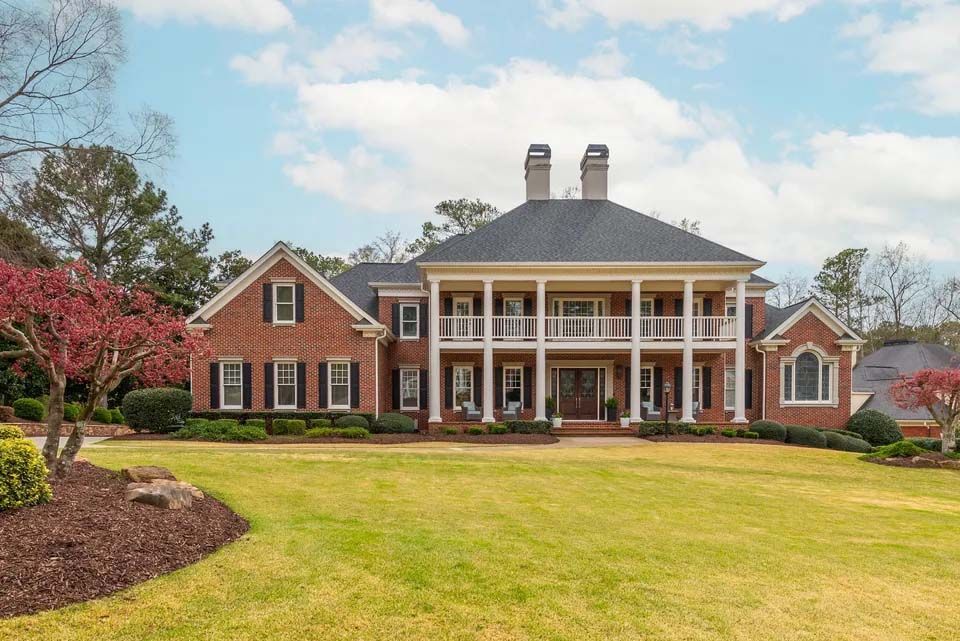 Two-story brick house with white columns and a green lawn under a partly cloudy sky.