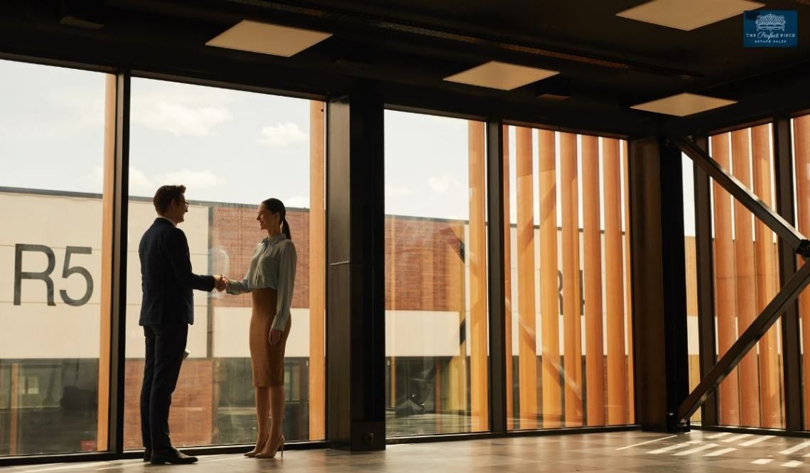 A man and a woman are shaking hands in a room with a lot of windows.