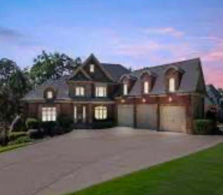 Large brick house with a driveway and attached garage, set against a colorful dusk sky.