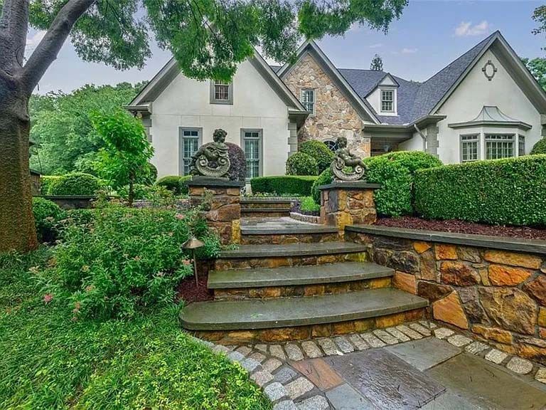 Stone steps leading up to a large house with a stone and stucco facade, surrounded by manicured landscaping.