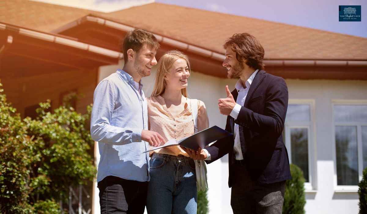 A man is talking to a couple in front of a house.