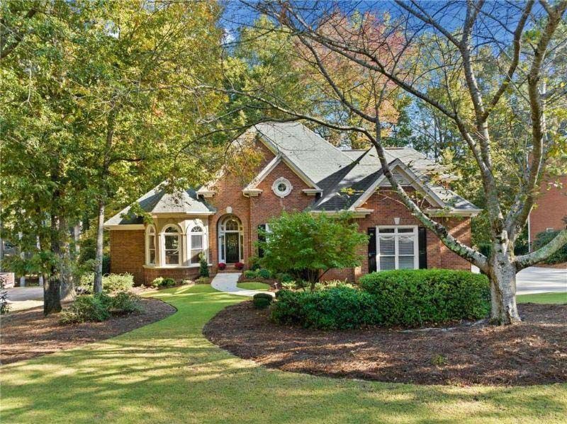 Brick house with landscaping, surrounded by trees, on a sunny day.