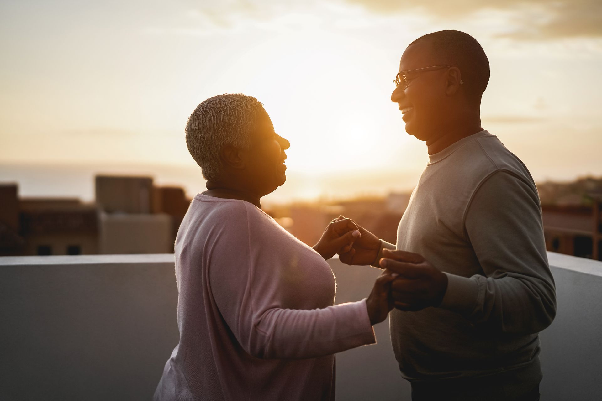 Couple dancing on a rooftop at sunset, holding hands, silhouetted against the sky.