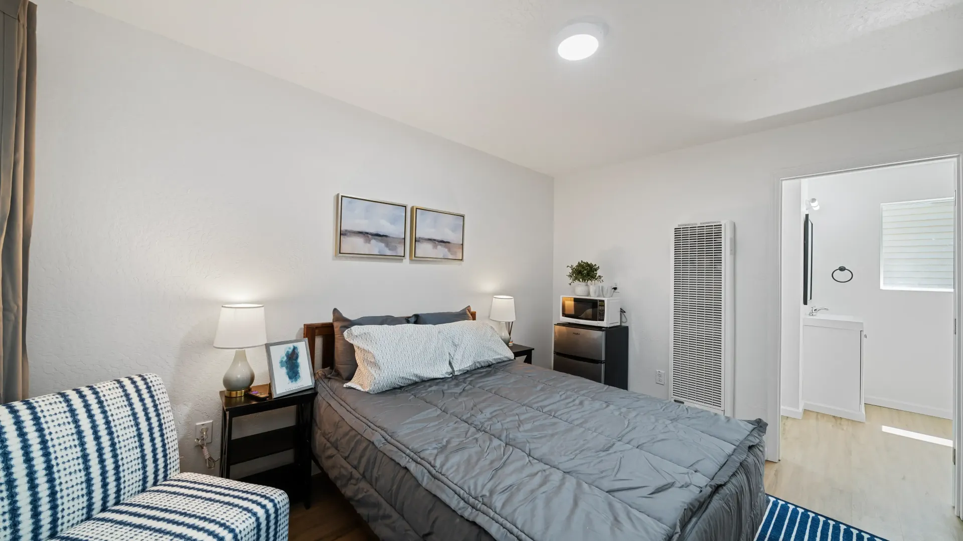 Bedroom with bed, armchair, art, and a small fridge by the wall.