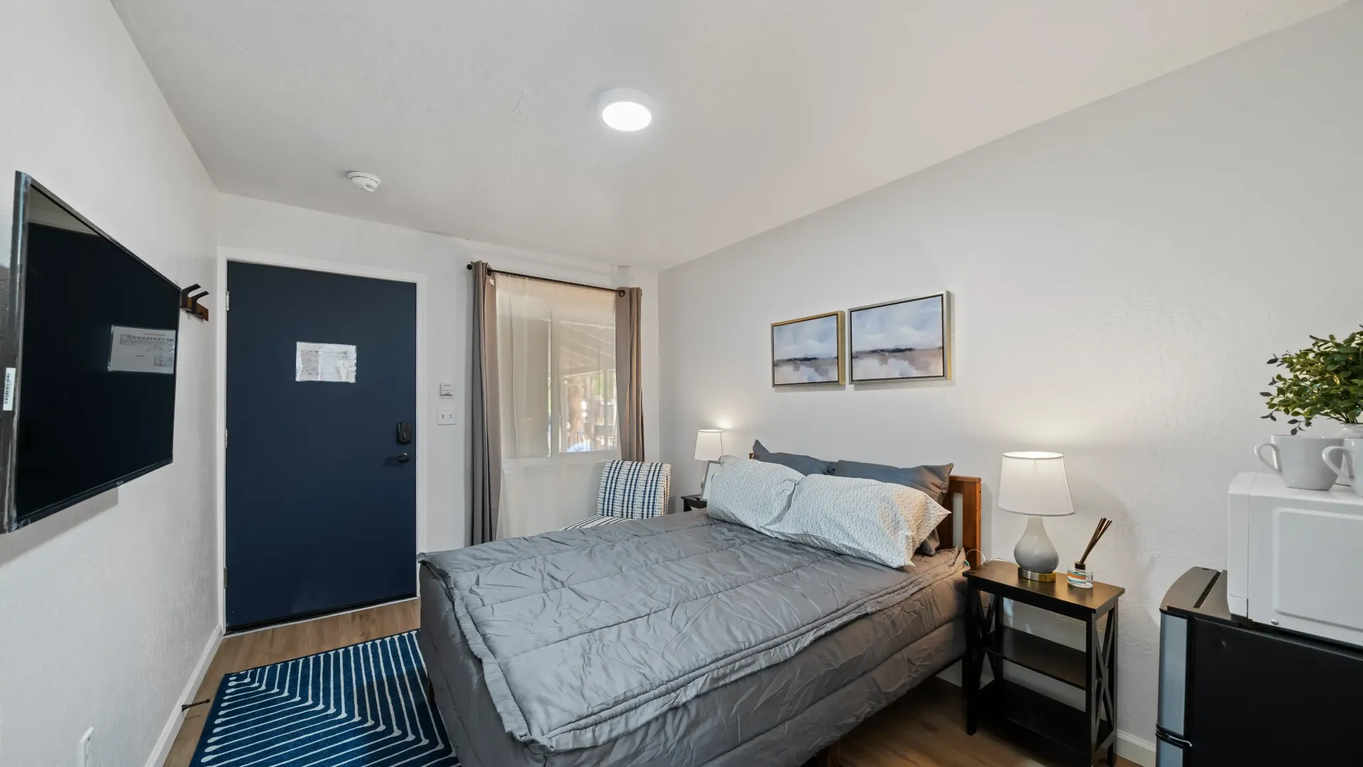 Small bedroom with bed, TV, blue door, and minimalist decor.