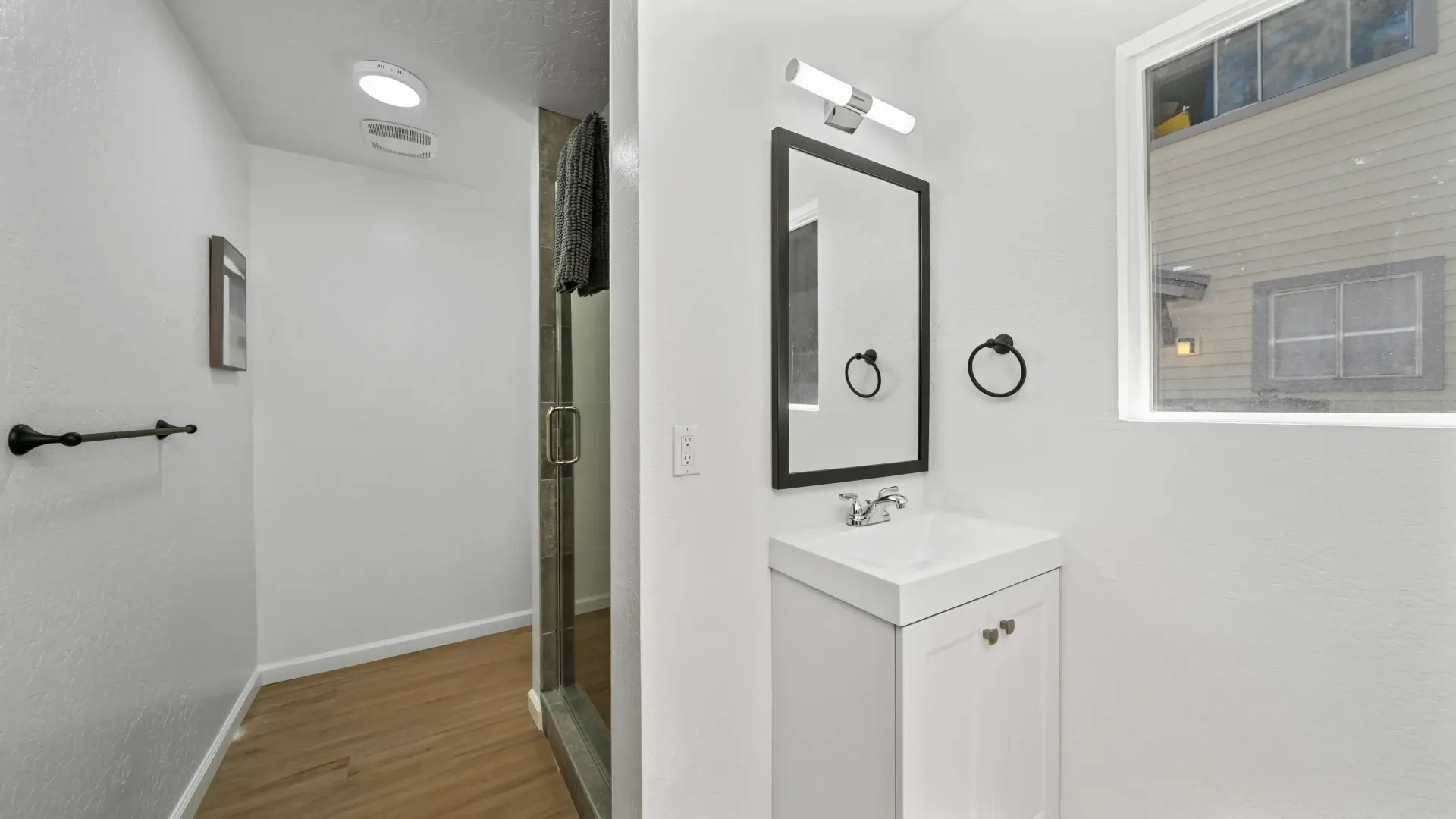 Small, white bathroom with a sink, mirror, and shower entrance.