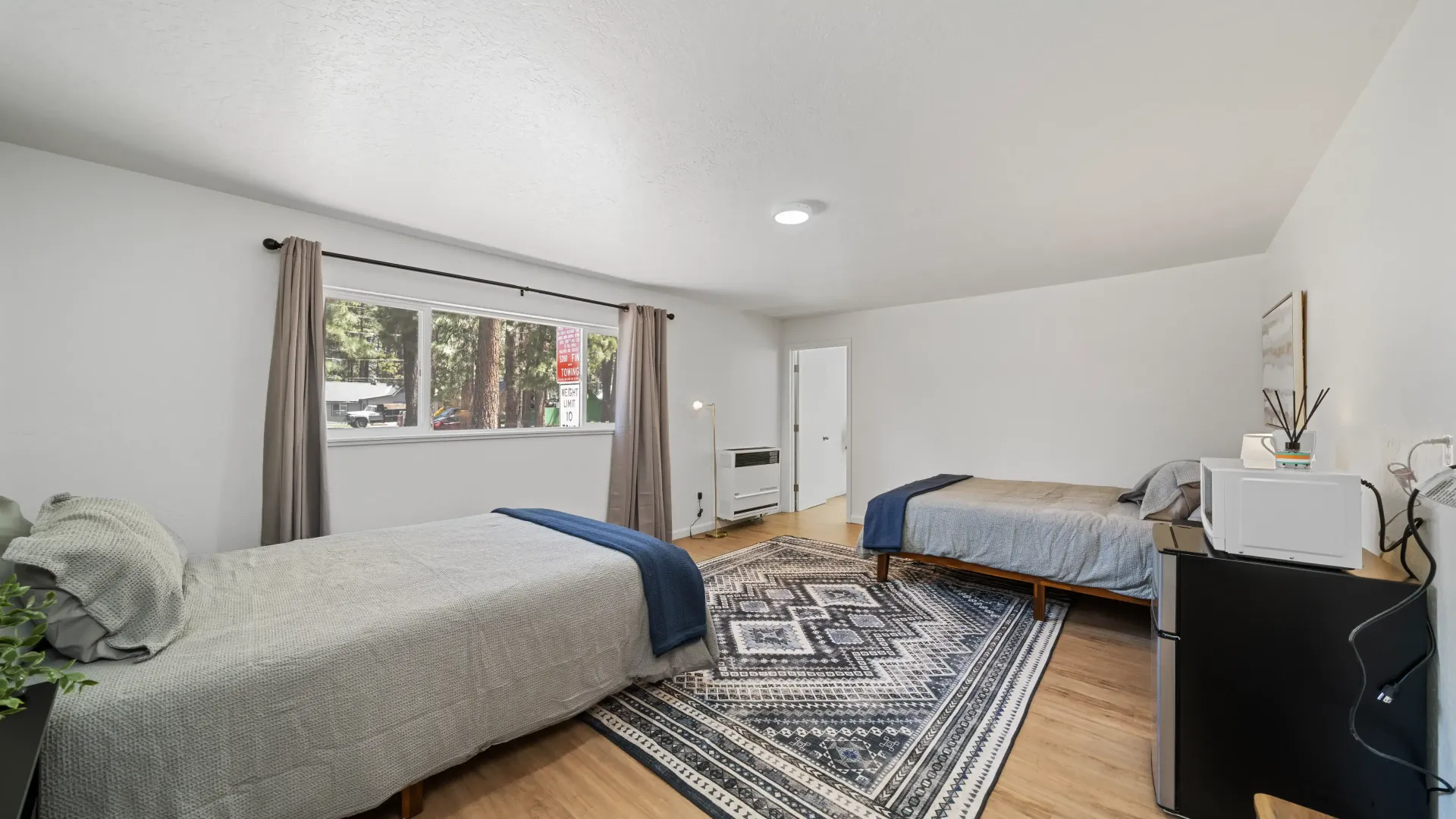 Two beds in a room with a window and rug. White walls, wooden floor.