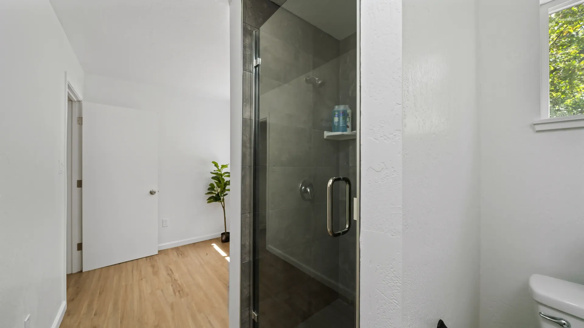 Bathroom interior with a glass shower, white walls, and wooden floor.