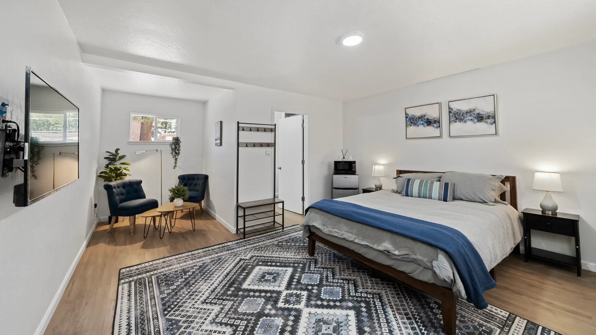 Bedroom with a bed, rug, two blue chairs, and a small table.