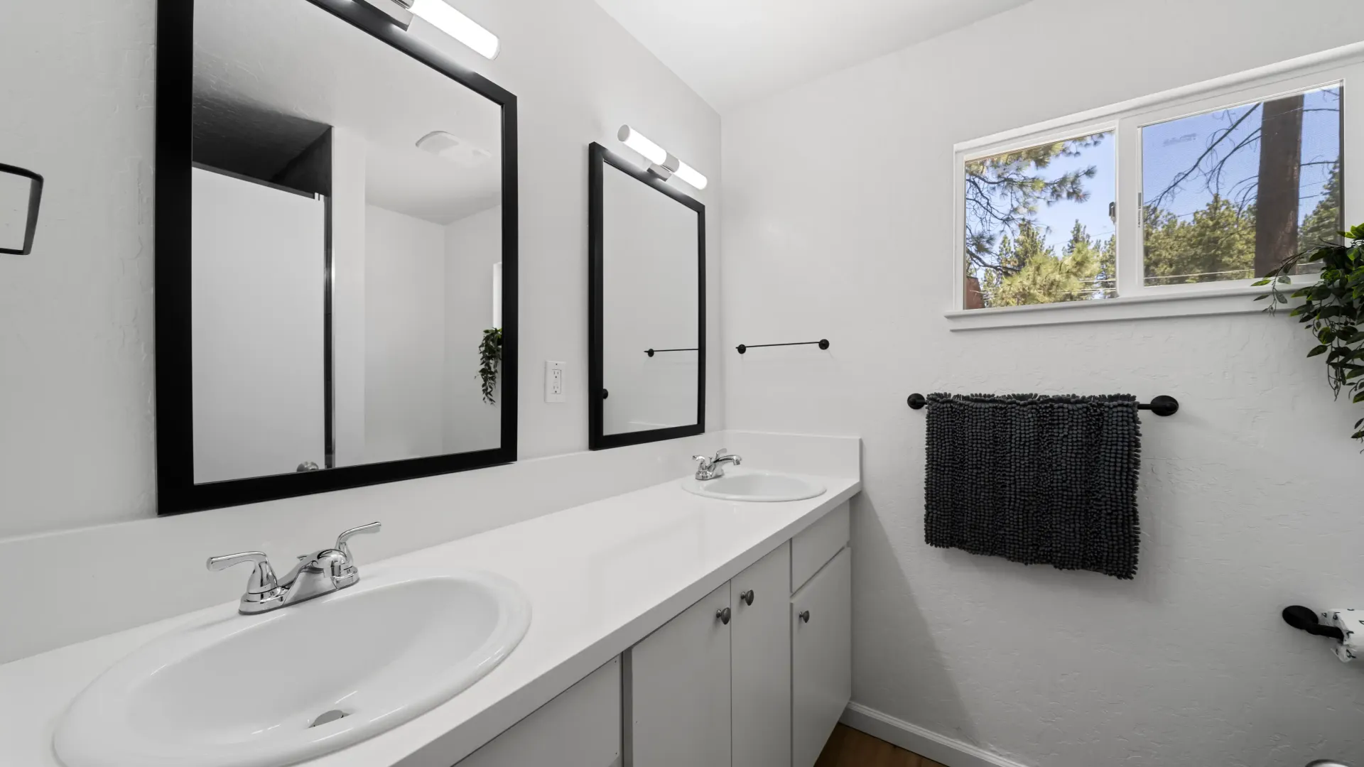 Bathroom with dual sinks, white cabinets, and black-framed mirrors. Includes a window and a towel rack.