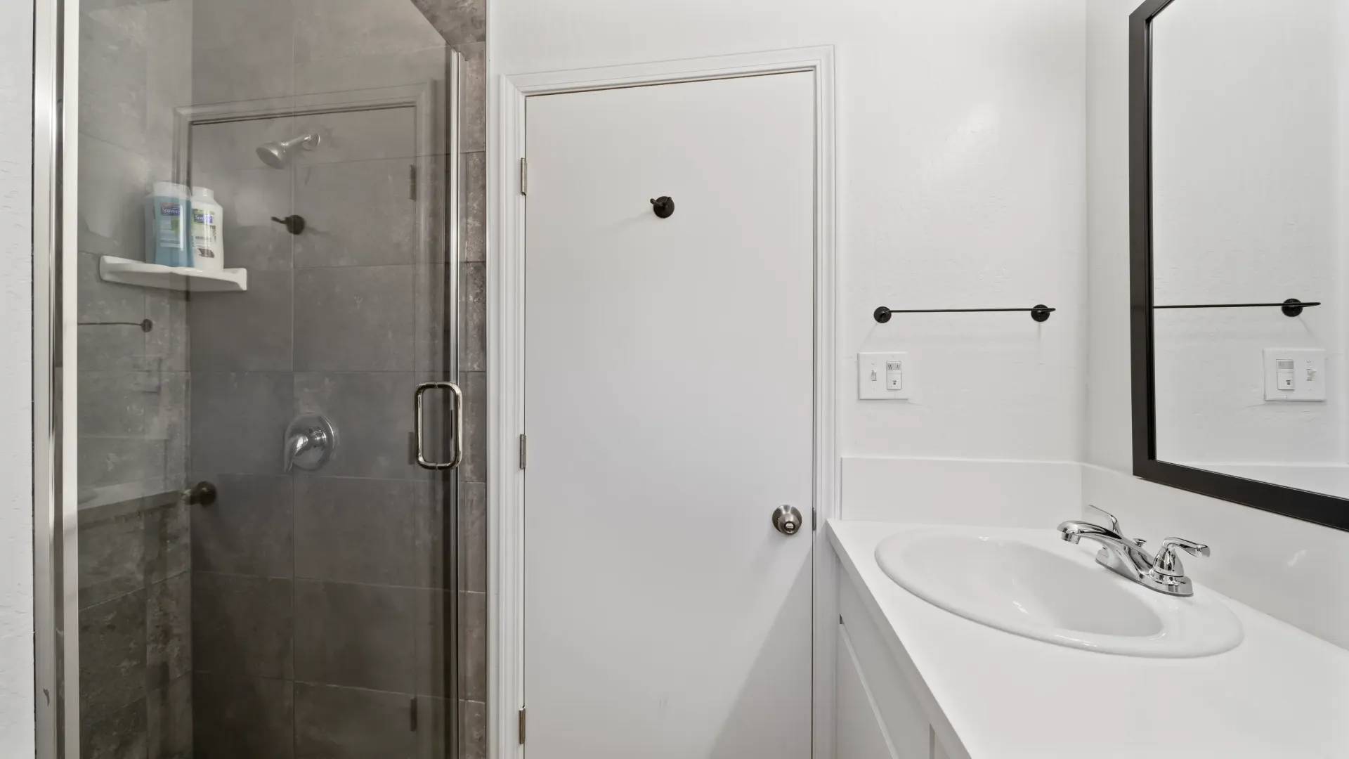 Bathroom with glass shower, white door, vanity, and mirror.