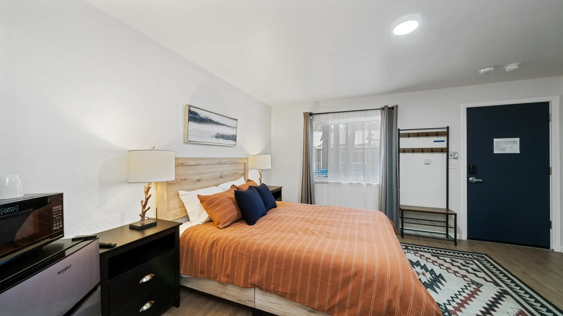 Bedroom with bed, bedside table, art, window, and dark blue door.