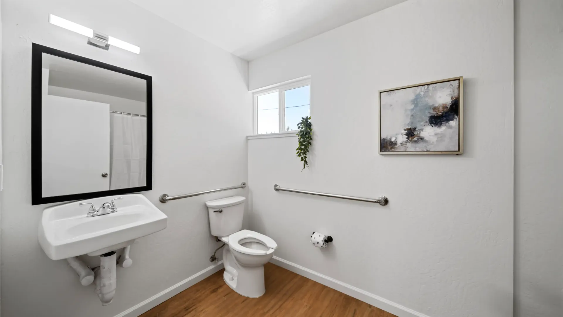 Accessible bathroom with sink, toilet, grab bars, and abstract art.