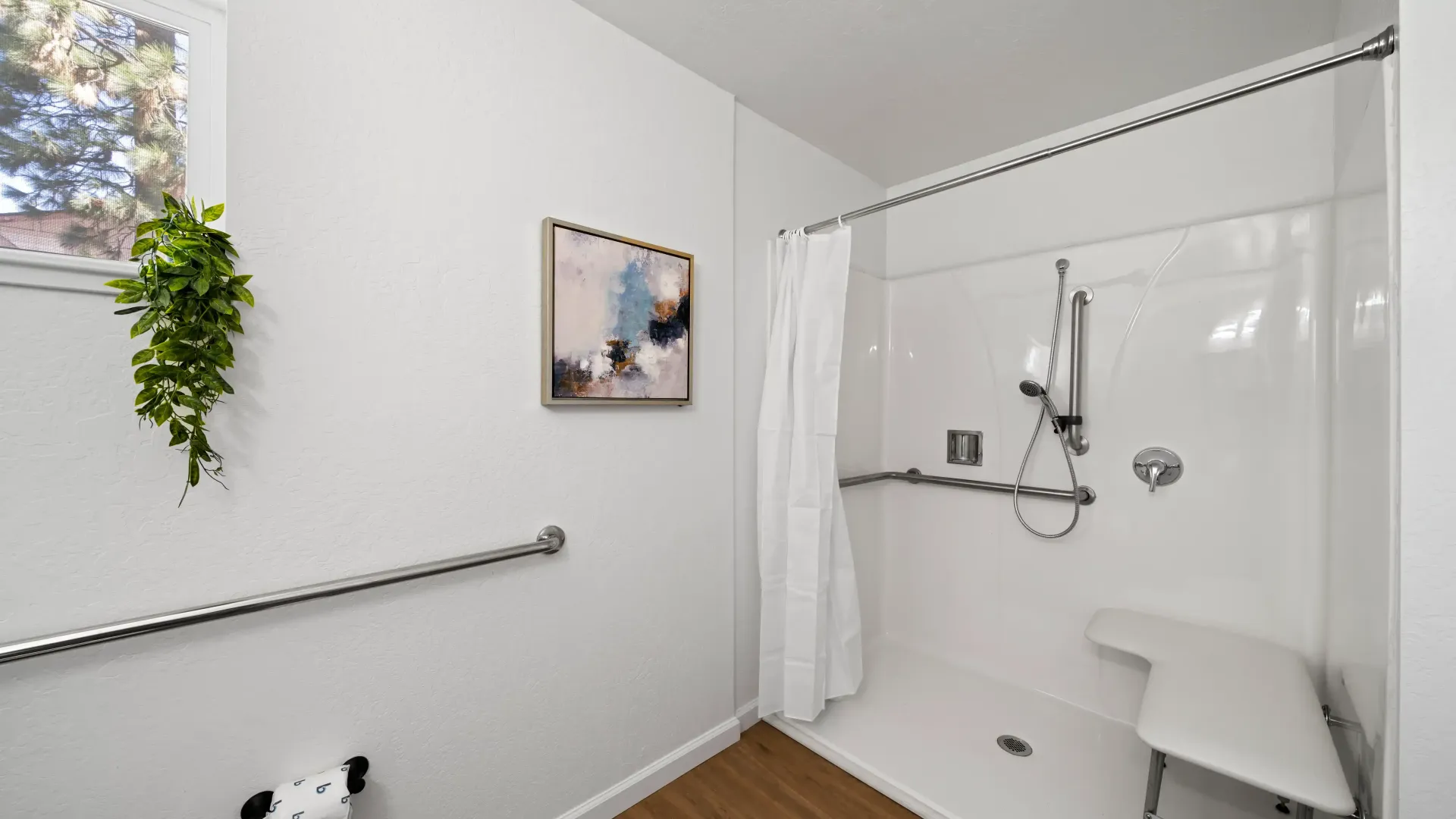 Accessible white bathroom with shower, grab bars, bench, and a small window.