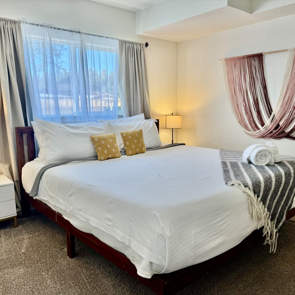 Bedroom with a bed, pillows, window, curtains, a lamp, and decorative wall hanging.
