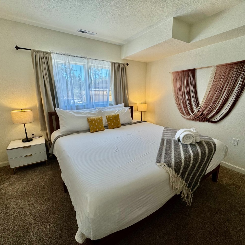 Bedroom with a bed, bedside tables, lamps, window, and decorative wall hanging.