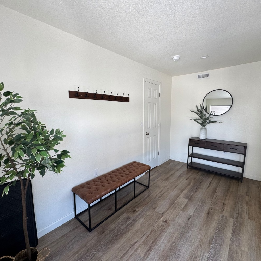 Hallway with wooden floors, bench, coat rack, console table, and a round mirror.