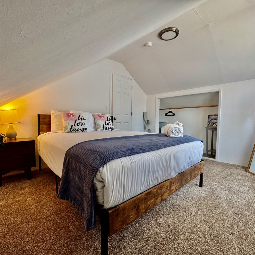 Bedroom with bed, nightstand, closet. White walls, brown carpet, and a blue blanket.