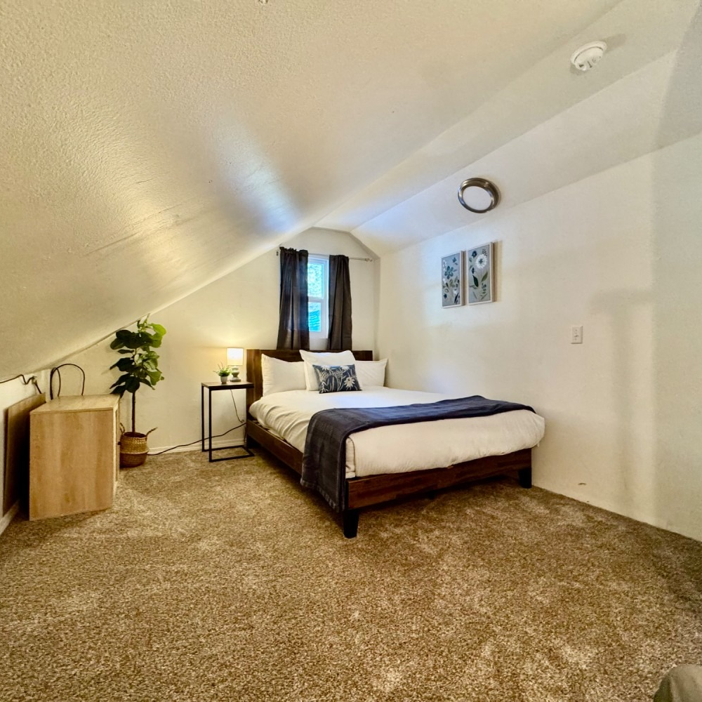 Bedroom with a bed, nightstand, and dresser in an angled-ceiling room; brown carpet and white walls.