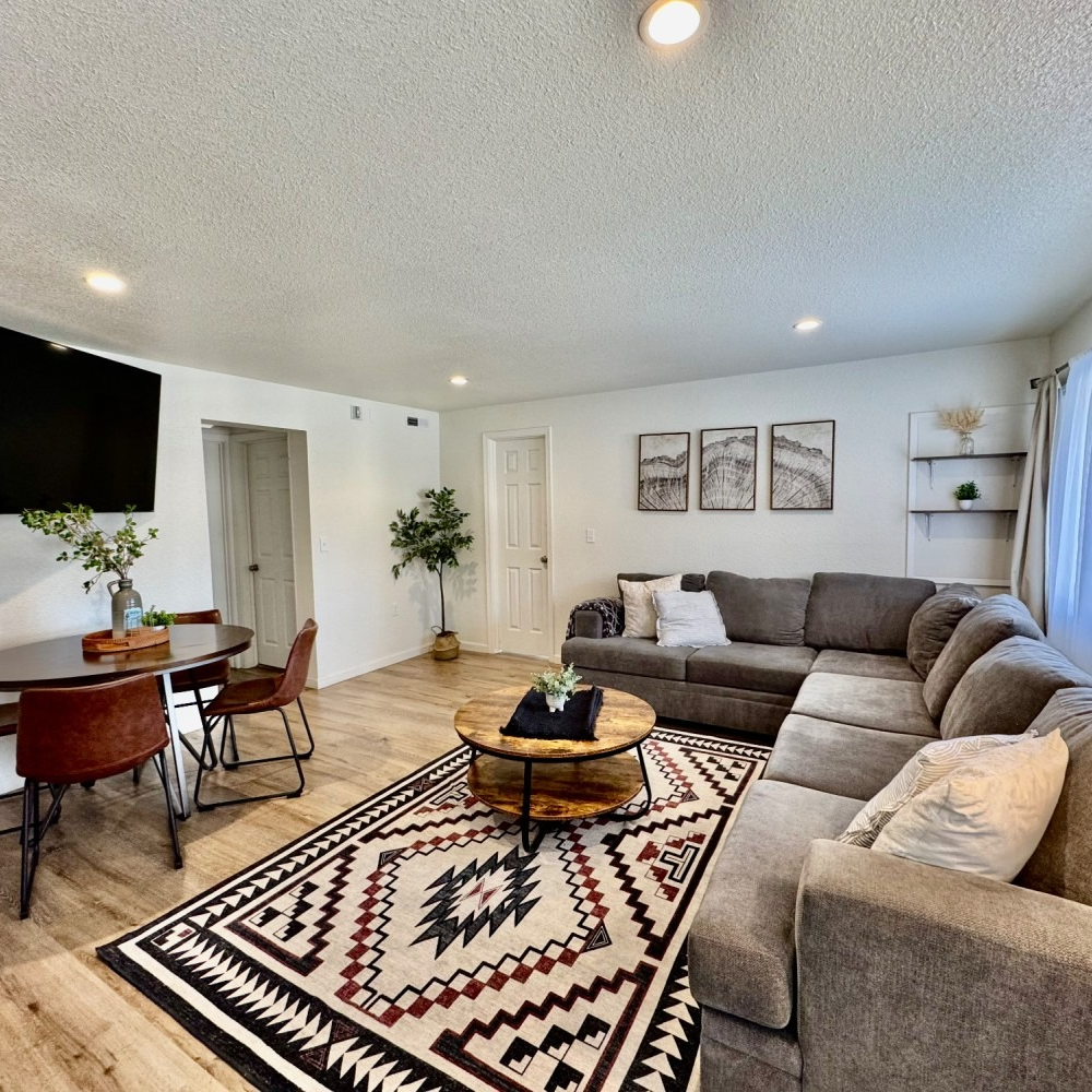 Living room with sectional sofa, dining table, area rug, and art on the wall.