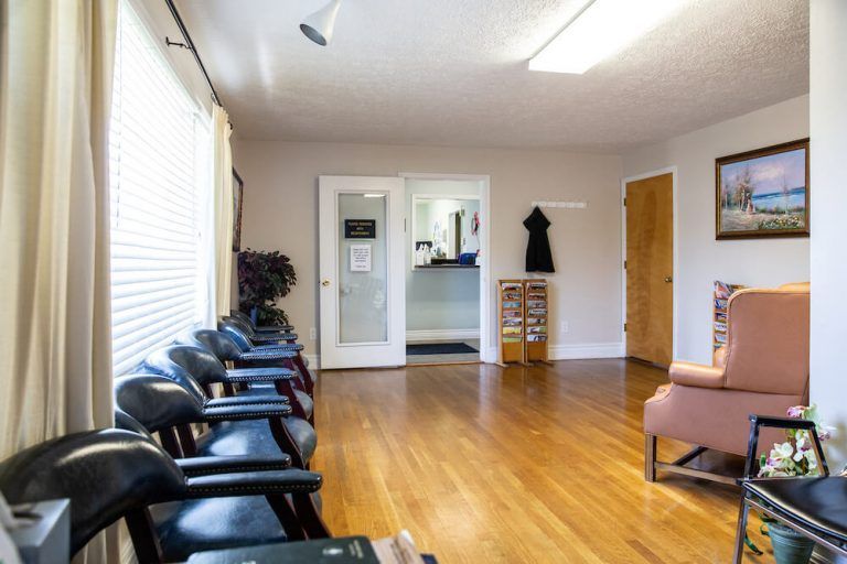 Waiting room with chairs, a pink armchair, and a view into an office.