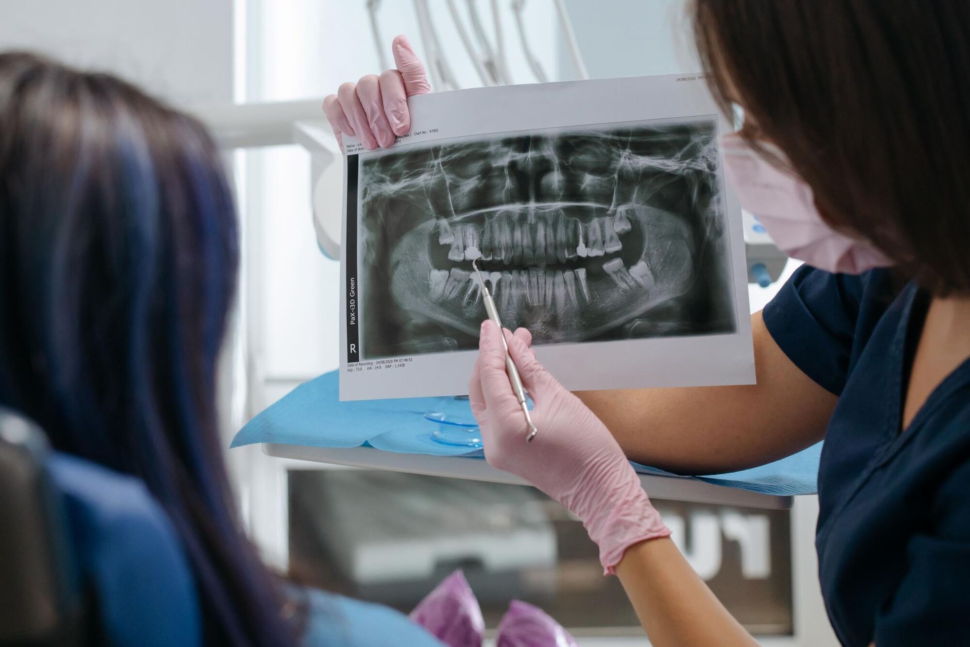 Dentist showing a patient’s X-ray while wearing pink gloves in a clinic