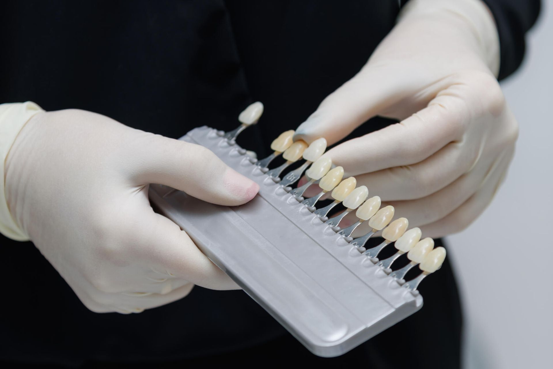 Gloved hands holding a dental shade guide for matching tooth colors