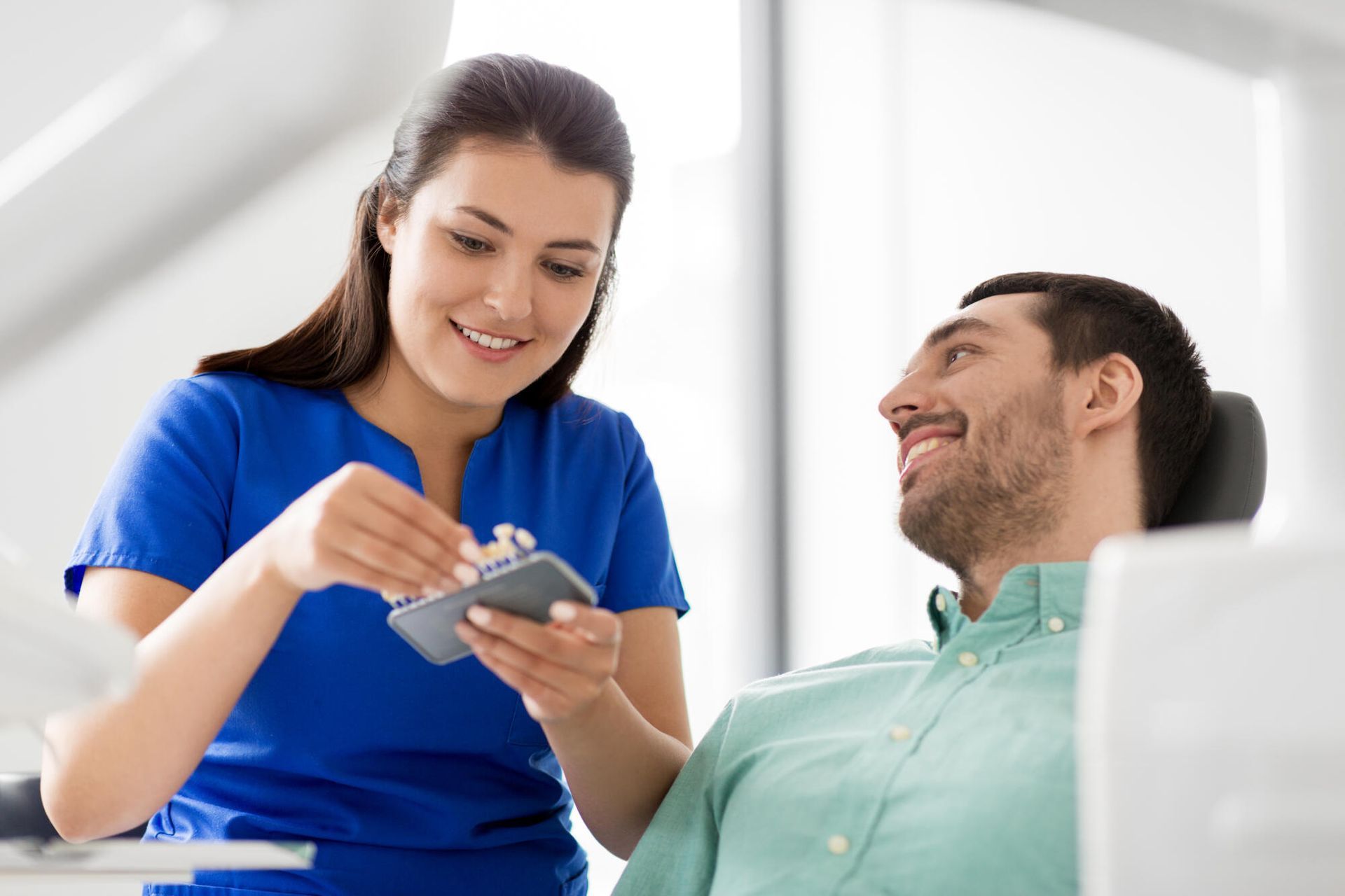 Dental hygienist showing a patient a set of teeth models in a dentist's office.
