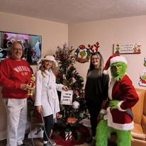 Four people in front of a Christmas tree, one dressed as The Grinch.