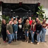 Group of people posing outside; woman with plants behind.