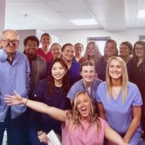 Group of diverse people smiling, posing indoors. Some wear scrubs.