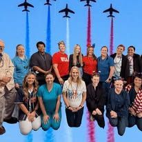 A group of people in front of jets in formation, in the sky.