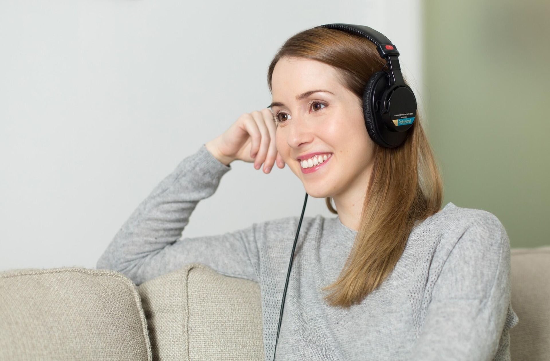 Woman sitting on a couch wearing headphones and smiling.