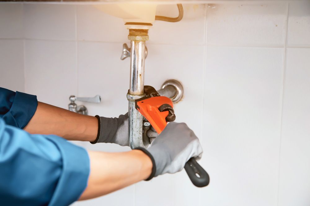 Plumber Using A Wrench To Repair A Water Pipe Under The Sink