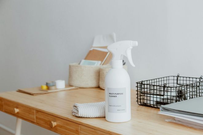 A white spray bottle sits on a light wood desk.
