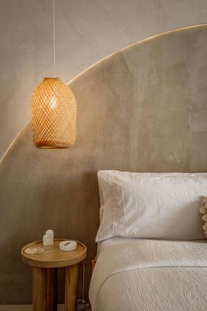 A textured woven pendant lamp hangs above a small wooden side table. A textured woven pendant lamp hangs above a small wooden side table.
