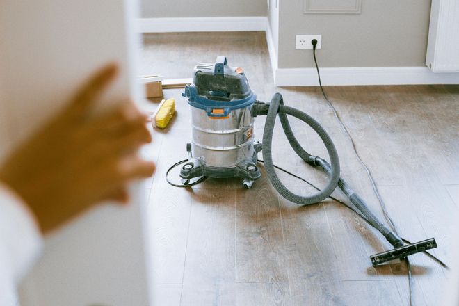 A shop vacuum sits on a wooden floor in a room.