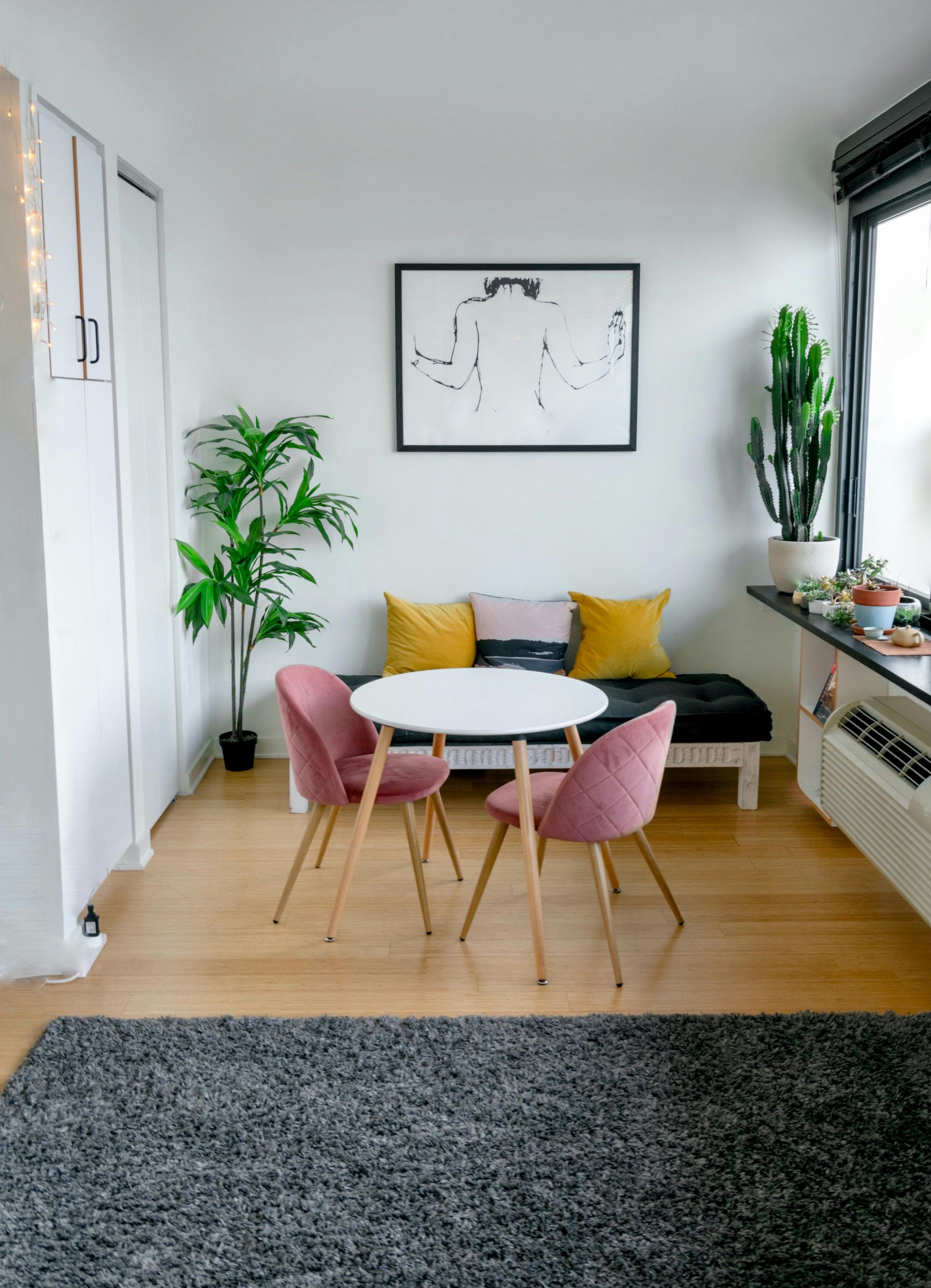 A modern dining nook with two pink chairs, a white table, and a sofa.