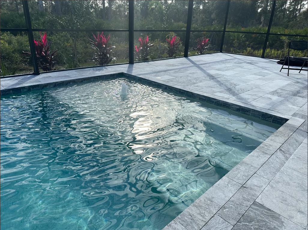 A large swimming pool is surrounded by palm trees and a body of water.