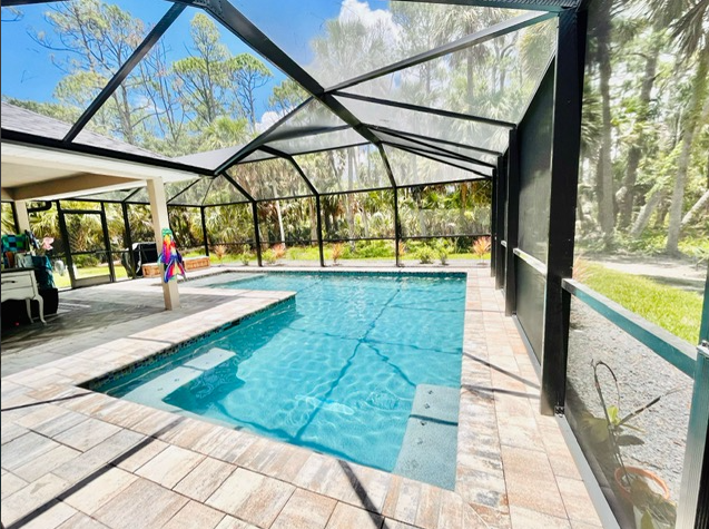 A large swimming pool is surrounded by a screened in area.