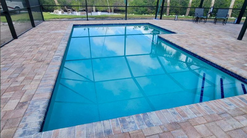 A large swimming pool is surrounded by a screened in area.