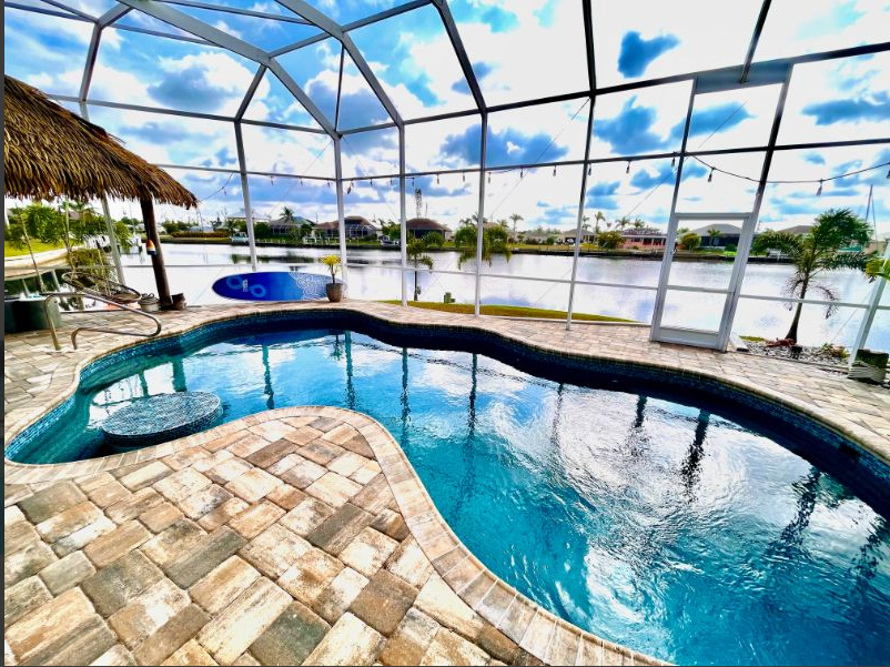 A large swimming pool is surrounded by a screened in area.